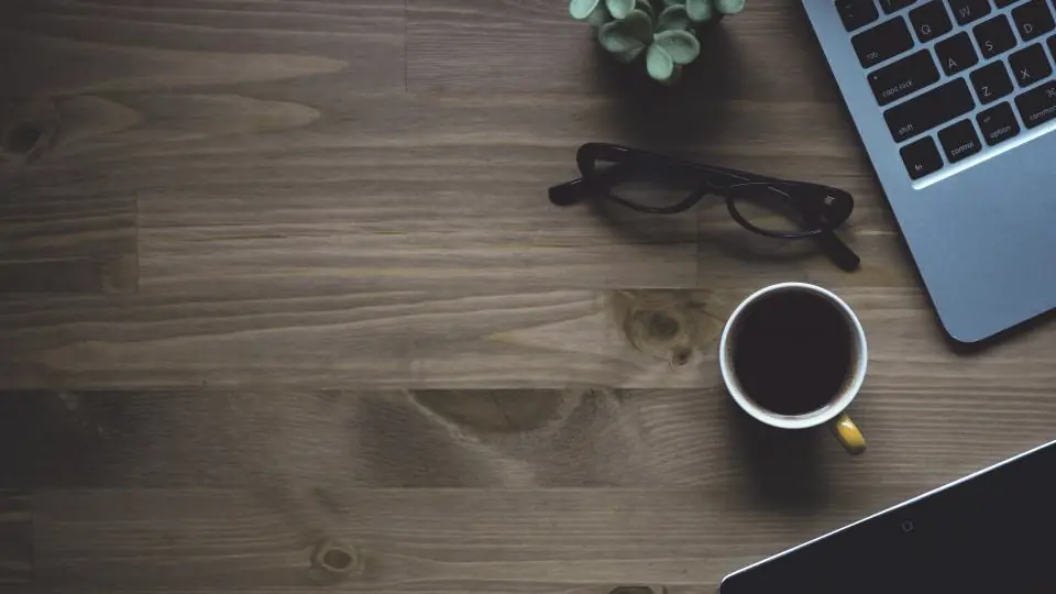 Escritorio de madera con notebook, anteojos y café visto desde arriba